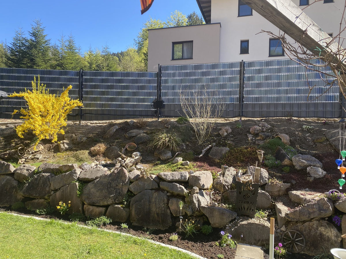 Sunbooster VERTICAL+ Solarzaun hinter einem Steingarten